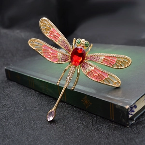 Vintage dragonfly brooch with red crystal and pink enamel on a classic dark book