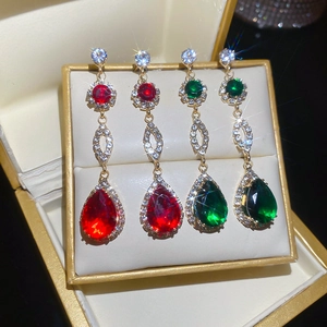Detail of elegant teardrop earrings with red and green gems in a golden jewelry box