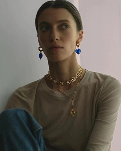Detailed view of blue heart glass earrings and layered gold necklaces on a model