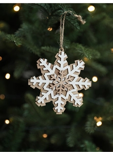 Close-up of dual-layer wooden snowflake ornament hanging on a warm Christmas tree branch