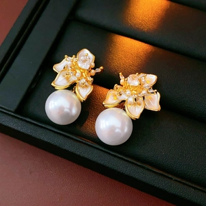 Detail of flower stud earrings with gold petals, sparkling rhinestones and white pearls