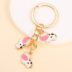 Close-up of golden keychain featuring three white enamel cows with cute black spots