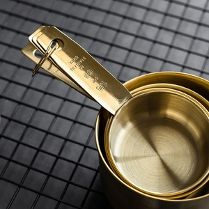 Golden stainless steel measuring cup set on black grid, showing 1/4 cup 60ml detail