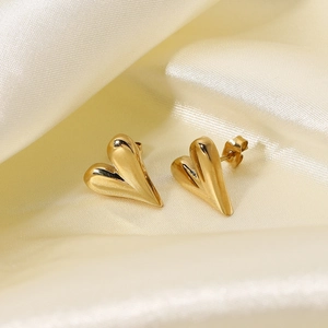 Macro shot of polished 14K gold-plated heart-shaped stud earrings on beige silk fabric