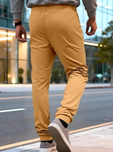 Street view of camel jogger pants with elastic cuffs and zippered pockets from a back angle