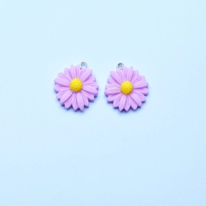 Detail of two purple resin daisy charms with yellow centers and silver hooks for jewelry