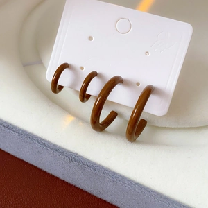 Close-up of four minimalist brown C-shaped drip glaze hoop earrings on a display card