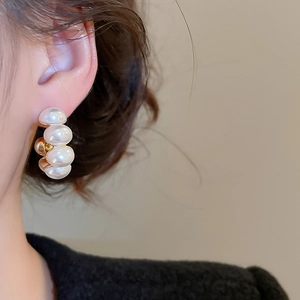 Detail view of C-shaped gold-plated earrings with four graduated white pearls on a model