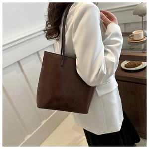 Detail of a dark brown leather tote bag styled with a white blazer in a minimalist setting