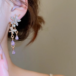 Close-up of golden floral earrings with rhinestones and purple teardrop gemstones