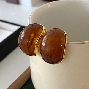 Minimalist 18k gold plated amber resin oval stud earrings on a white ceramic cup