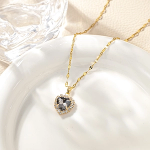 Macro detail of heart-shaped necklace with grey gemstone and gold chain on ceramic plate