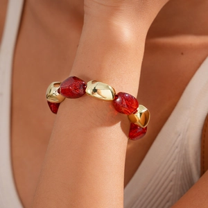 Detail of red glitter acrylic beads and polished gold metal charms on a wrist bracelet