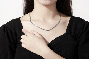 Gros plan d'un collier chaîne serpent plate argentée porté sur un pull noir côtelé
