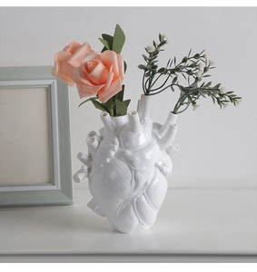 Detail of anatomical heart vase in white ceramic with pink roses and green leaves