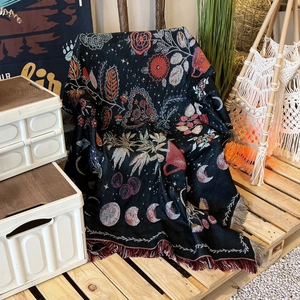 Detail of bohemian woven blanket featuring moon phases and floral patterns with red tassels