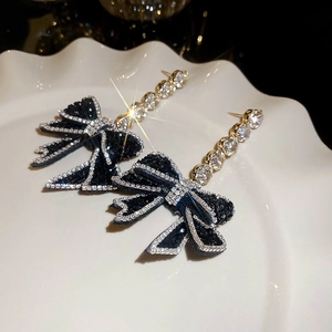 Macro detail of long silver drop earrings with black bow and sparkling crystals