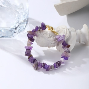 Detailed close-up of natural amethyst chips bracelet with golden lobster clasp on white marble