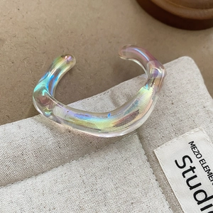 Detailed macro view of an iridescent acrylic irregular geometric wave ring on beige fabric