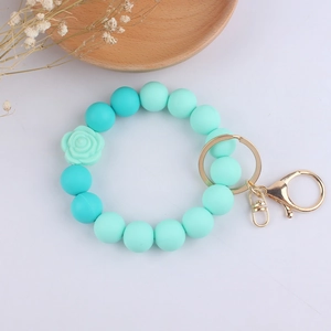 Detail of beaded silicone bracelet keychain with teal floral charm and gold metal ring