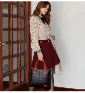 Chic embossed leather tote bag with red handles shown in a lifestyle street setting