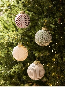 Close-up of vintage white Christmas ornaments with embossed patterns on a lit tree