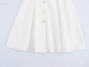 Detailed close-up of white pleated A-line skirt featuring decorative gold front buttons