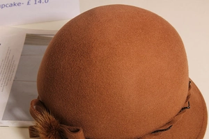 Detail of wool cloche hat with brown fur ball, bow ribbon and black bead chain decor