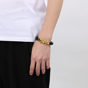 Détail d'un bracelet en cuir tressé noir avec trois crânes dorés sur poignet masculin