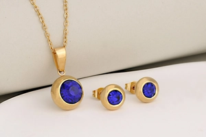 Close-up of gold-plated stainless steel jewelry set with round blue birthstone crystals