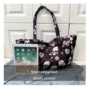 Large black punk tote bag with skull and floral print shown next to an iPad for size comparison
