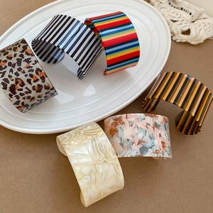 Close-up of six wide acrylic C-shaped open bracelets in various patterns on a ceramic plate