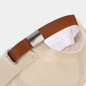 Detailopname van de beige katoenen pet met bruine lederen riem en een zilveren gesp