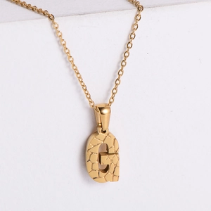 Macro detail of 18K gold plated letter G necklace with unique hammered stone texture finish