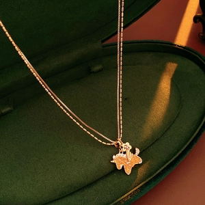Detailed close-up of a gold pony pendant necklace on green velvet gift box