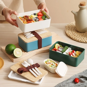 Three-color Japanese bento boxes with bamboo lids and elastic cutlery straps on wood