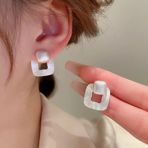 Detail of brushed silver square earring with a pearl center inlay on a female model