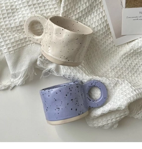 Detailed view of beige and purple ceramic ink-splatter mugs with unique ring handles