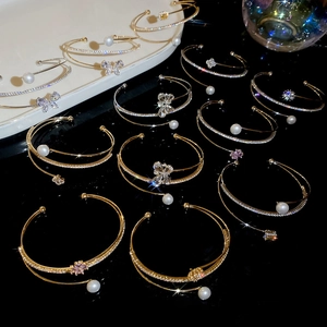 Close-up of gold open bangles with pearls and flower zircon charms on a black surface