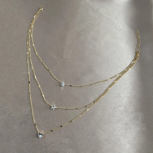 Three-layer gold necklace with crystal teardrop, star, and heart pendants on fabric