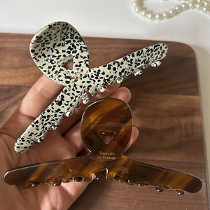 Large acetate hair claws in leopard and amber patterns with gold logo on wood background