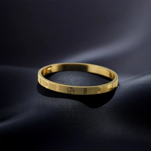 Detail of gold titanium steel bangle with Greek key patterns and textured finish