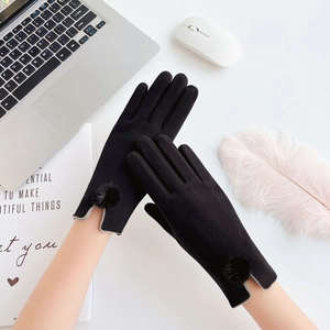 Detail of black winter touchscreen gloves with rabbit fur pom-poms on a white desk