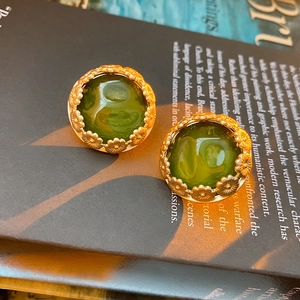 Detail of vintage round dark green earrings with gold flower frames on a book
