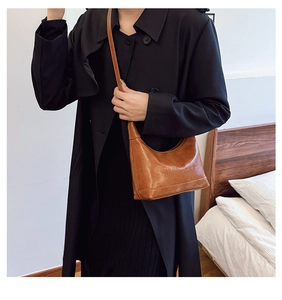 Detail of a brown crescent-shaped leather crossbody bag with embossed patterns and thin strap