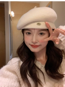 Detailed close-up of cream wool beret featuring a metallic ML letter emblem on the side