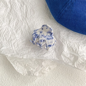 Detail of blue and white porcelain pattern hair claw clip on white textured backdrop