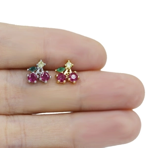 Macro detail of cherry-shaped nose studs in gold and silver finish with red zircon