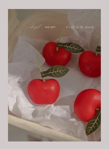Primer plano de cuatro velas aromáticas con forma de cereza roja y etiquetas de hojas