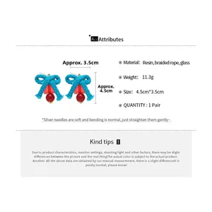 Close-up of blue braided bow earrings with translucent red resin and glass pendants
